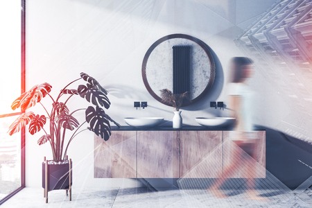 Young woman walking in stylish bathroom interior with double sink standing on wooden countertop and round mirror. Toned image double exposure blurの写真素材