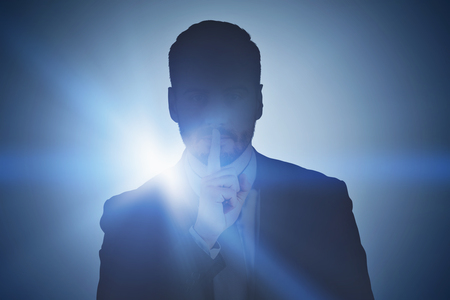Portrait of handsome young man in suit standing with finger near his lips. Dark background. Concept of keeping a secret. Toned imageの写真素材