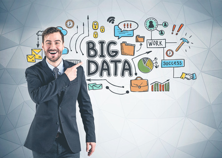 Happy young businessman in suit pointing at colorful big data sketch drawn on gray wall with geometric pattern.の写真素材