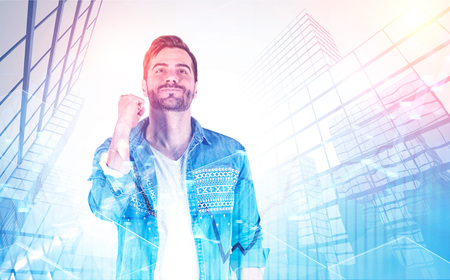 Smiling man in casual clothes celebrating financial victory over modern city background with double exposure of graphs. Startup concept. Toned imageの写真素材