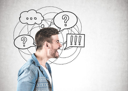 Side view of angry man shouting standing near concrete wall with question and exclamation marks in speech bubbles. Concept of unsolved questions. Mock upの写真素材
