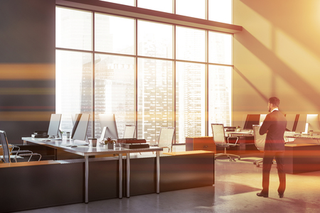 Bearded businessman standing in office with gray walls and rows of yellow and gray computer tables. Toned imageの写真素材