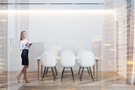 Blonde businesswoman standing in minimalistic white dining room interior with wooden floor and white table with chairs. Toned image double exposureの写真素材