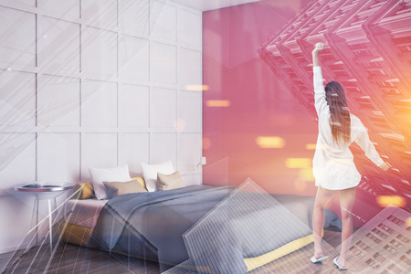 Rear view of woman in nightgown standing in stylish bedroom interior with red and white walls, wooden floor and yellow master bed. Toned image double exposureの写真素材