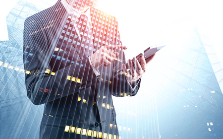 Unrecognizable businessman using digital tablet over skyscraper background. Concept of modern technology. Toned image double exposureの写真素材