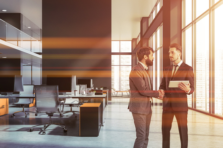 Two businessmen shaking hands in office interior with gray walls and rows of computer desks. Toned imageの写真素材