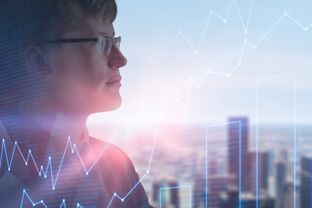 Side view of serious businessman in glasses over blurred city background with double exposure of graphs. Stock market concept. Toned imageの写真素材