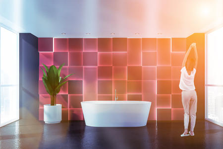 Woman in pajamas standing in modern luxury bathroom with red and gray walls, comfortable bathtub and big potted plant. Toned imageの写真素材