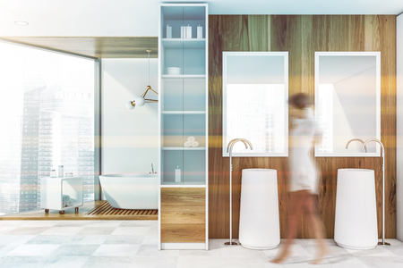 Young woman walking in luxury bathroom with wooden walls, large window, comfortable bathtub and double sink with mirrors. Toned image blurredの写真素材