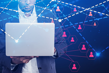 Serious African American businessman holding laptop with double exposure of social network icons....