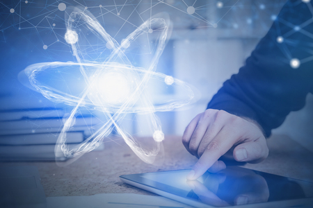 Hand of man using tablet computer in office with double exposure of atom hologram. Concept of scientific research and hi tech. Toned imageの写真素材