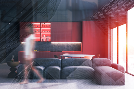 Young woman walking in concrete wall kitchen with red countertops, round table with chairs and soft gray sofa. Toned image double exposure blurredの写真素材