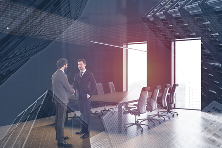 Two smiling young businessmen shaking hands in modern office conference room with brick and black walls and long meeting table. Concept of partnership. Toned image double exposureの写真素材