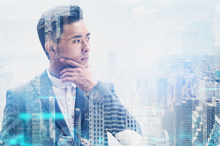 Young thoughtful Asian businessman looking at city with double exposure of network hologram. Concept of hi tech in businessの写真素材