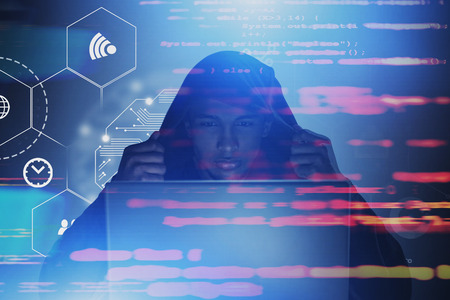 Serious African American hacker in hoodie looking at laptop. Double exposure of online security interface and blurred lines of code. Toned imageの写真素材