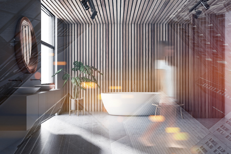 Young woman walking in modern bathroom with gray and wooden walls, white bathtub and double sink with round mirror above it. Toned image double exposure blurredの写真素材