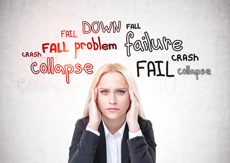 Stressed blonde woman in suit sitting near concrete wall with failure words written on it. Concept...