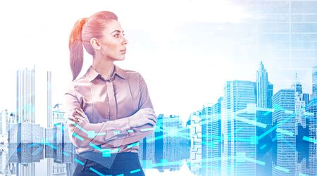 Confident European businesswoman standing with crossed arms over cityscape background with double exposure of graphs. Stock market concept. Toned imageの写真素材