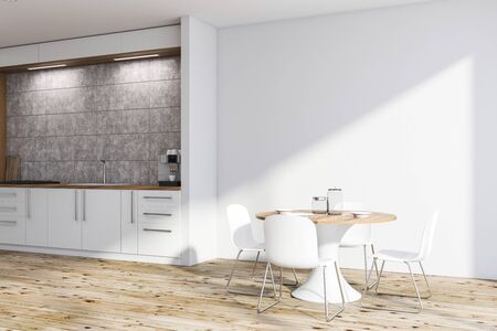 Corner of stylish kitchen with white and concrete walls, wooden floor, white countertops and round...