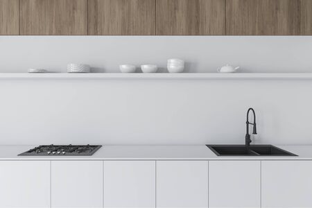 Close up of white countertops with built in sink and cooker with shelf for dishes above it standing...