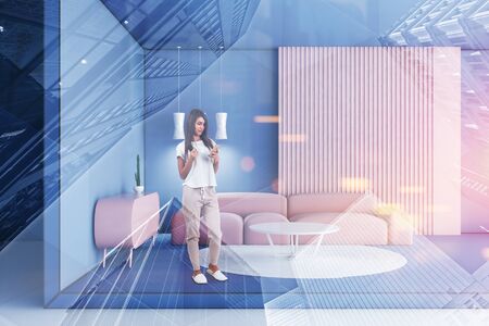 Woman with phone standing in modern living room with blue and pink walls, pink sofa near white coffee table and stylish cabinet. Toned image double exposureの写真素材