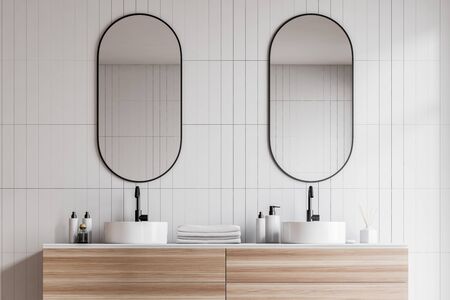 Close up of double bathroom sink standing on wooden countertop with towels on it and oblong mirror above it in room with white tile walls. 3d renderingの写真素材