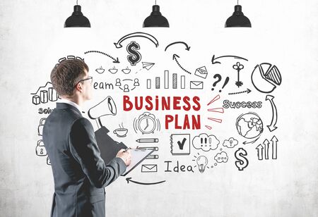 Side view of young businessman with clipboard looking at concrete wall with business plan sketch drawn on it. Concept of business analysisの写真素材