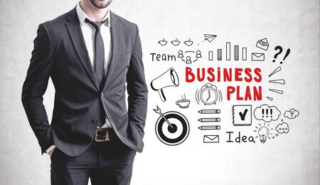 Confident businessman standing with hands in pockets near concrete wall with business plan sketch drawn on it.の写真素材