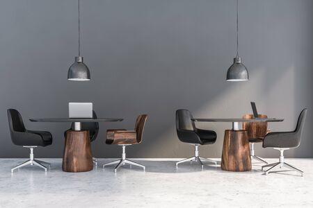 Interior of coworking office with gray walls, concrete floor, round tables with laptops and black and wooden chairs near them. 3d renderingの写真素材