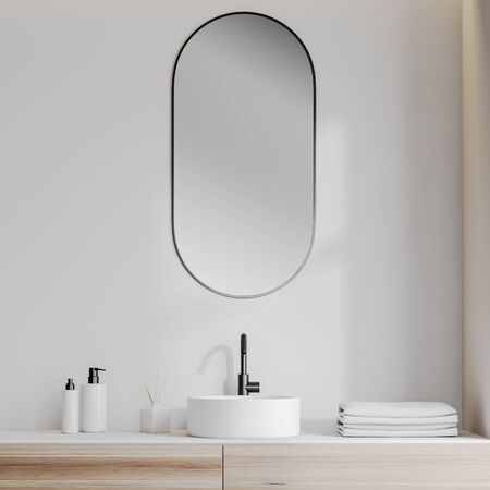Close up of white bathroom sink standing on wooden counter with oblong mirror above it in room with white walls. 3d renderingの写真素材