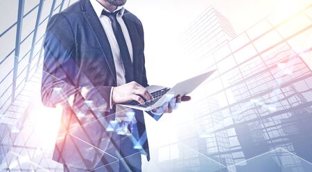 Unrecognizable businessman working with laptop over skyscraper background with double exposure of graphs. Concept of trading. Toned imageの写真素材