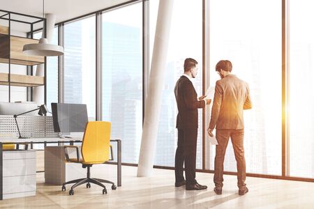Two businessmen discussing documents in panoramic office with white walls, wooden floor, white computer desk and wooden bookcase. Toned image double exposureの写真素材