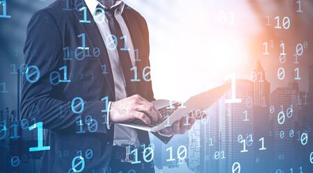 Unrecognizable man in suit using laptop in city with double exposure of binary numbers. Concept of...