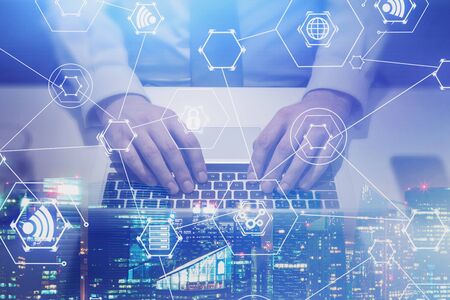 Top view of businessman typing on laptop at office table with double exposure of night cityscape and...