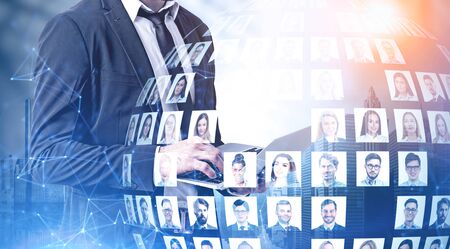 Unrecognizable businessman using laptop in city with double exposure of diverse people portraits and network hologram. Concept of social media. Toned imageの写真素材