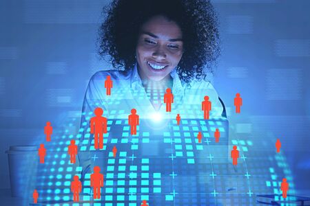 Smiling beautiful African American woman looking at laptop with double exposure of planet and people...