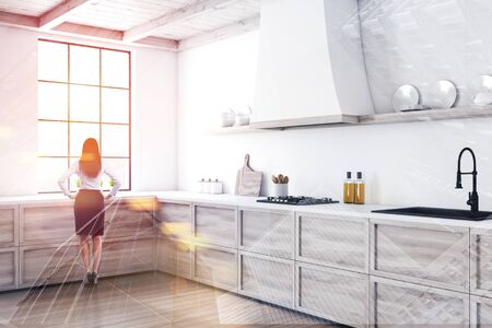 Woman in formal clothes standing in stylish kitchen interior with white walls, wooden floor and wooden countertops with built in sink and cooker. Toned image double exposureの写真素材