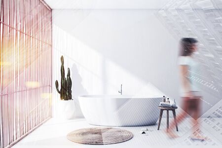 Young woman walking in modern bathroom with white walls, wooden blinds and comfortable white bathtub. Toned image double exposure blurredの写真素材