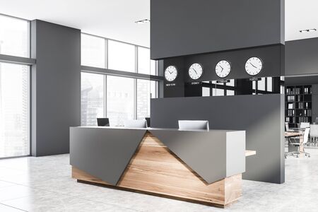 Corner of modern open space office with grey walls, tiled floor, rows of computer tables and gray and wooden reception table with clocks above it. 3d renderingの写真素材