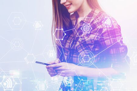 Smiling woman in casual clothes looking at smartphone over night city background with double exposure of hi tech interface. Concept of internet and communication. Toned imageの写真素材