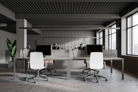 Interior of modern industrial style office with gray geometric pattern walls, concrete floor, columns and rows of gray computer tables with white chairs. 3d renderingの写真素材