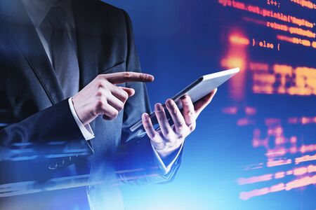Unrecognizable man in suit with tablet standing near virtual screen with code. Concept of...