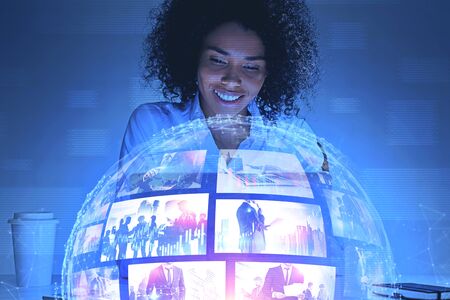 Smiling young African American woman looking at futuristic video streaming interface. Concept of hi tech and social media. Toned image double exposure. Elements of this image furnished by NASAの写真素材