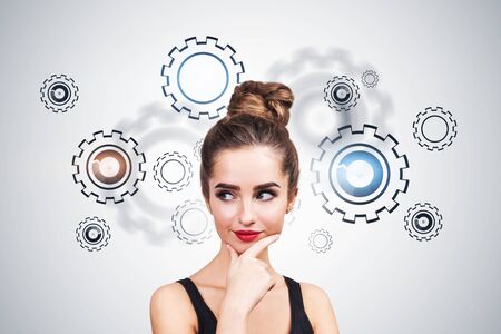 Thoughtful young woman in tank top standing near white wall with gears on it. Concept of...