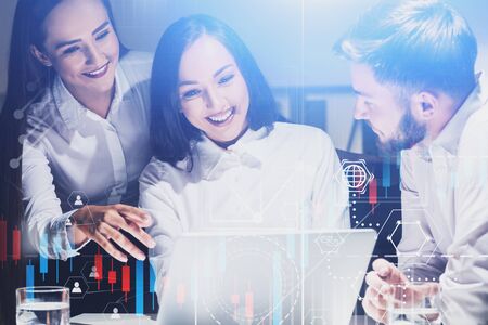Cheerful young business people working in office with laptop and double exposure of graphs and...