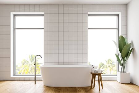 Interior of minimalistic bathroom with white tile walls, wooden floor, comfortable white bathtub and chair with towels and bottles. 3d renderingの写真素材