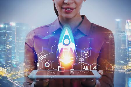 Smiling businesswoman with tablet standing in night city with double exposure of startup interface....