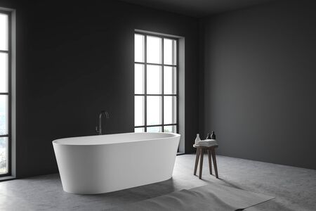 Corner of minimalistic loft bathroom with gray walls, concrete floor, large windows and comfortable white bathtub. Chair with towers and cosmetic products. 3d renderingの写真素材