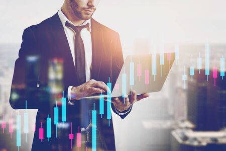 Businessman working with laptop in blurred city with double exposure of graphs. Concept of stock market. Toned imageの写真素材