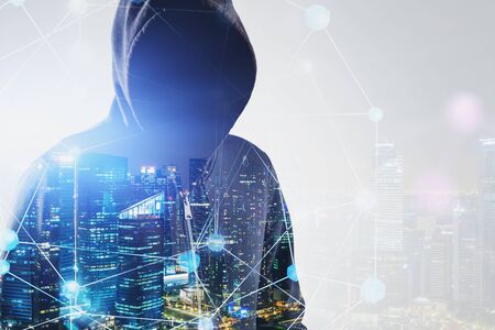 Close up of young hacker in hoodie standing in night city with double exposure of network interface....